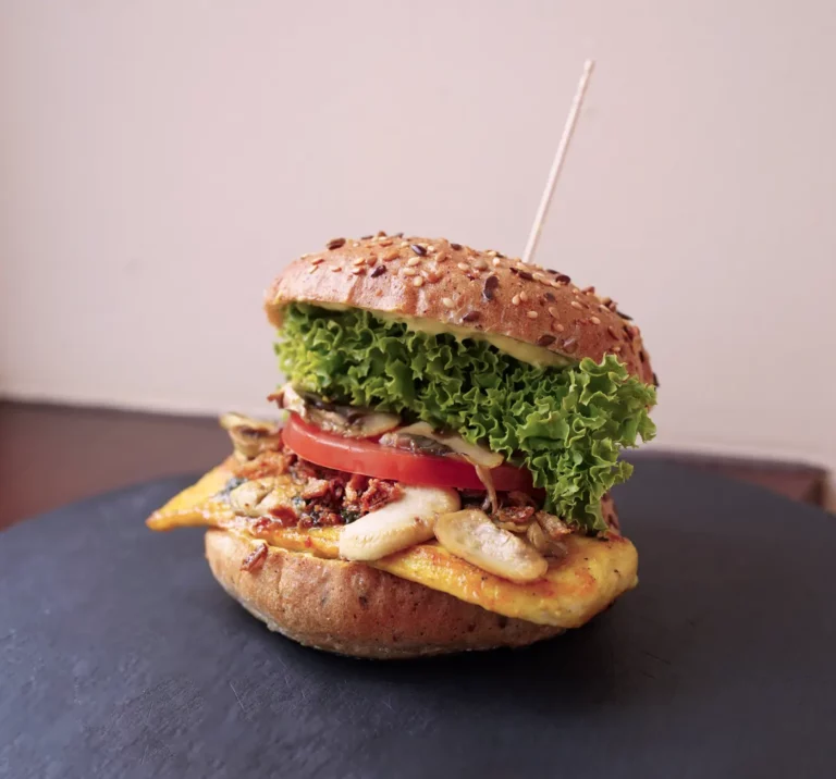 Unser Monatsburger im Juni 2025 heißt Maya und setzt sich aus gegrillter Hähnchenbrust, gebratenen Champignons, Basilikum-Pesto, Röstzwiebel, Tomaten und Salat zusammen